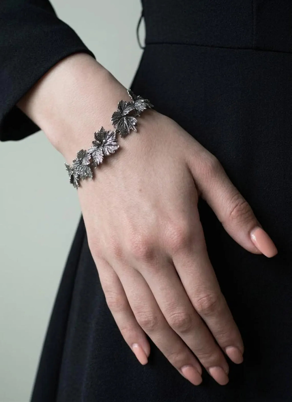 Hand wearing a decorative silver bracelet against a neutral background