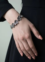 Hand wearing a decorative silver bracelet against a neutral background