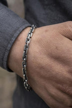 Close-up of a wrist wearing a silver chain bracelet with a blurred background
