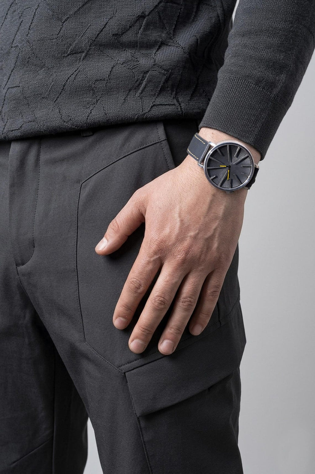 Person wearing a dark gray sweater and pants with a matching watch on a light gray background