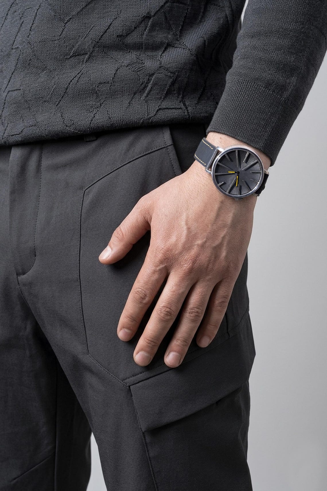 Person wearing a dark gray sweater and pants with a matching watch on a light gray background