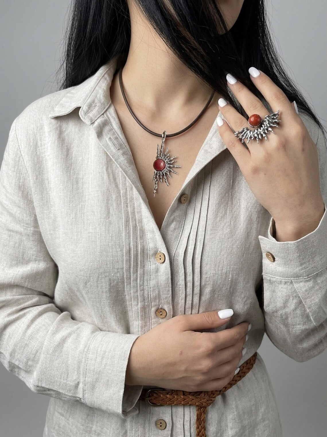 Person wearing a necklace and ring with a neutral background
