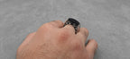 Hand wearing a black ring on a gray background
