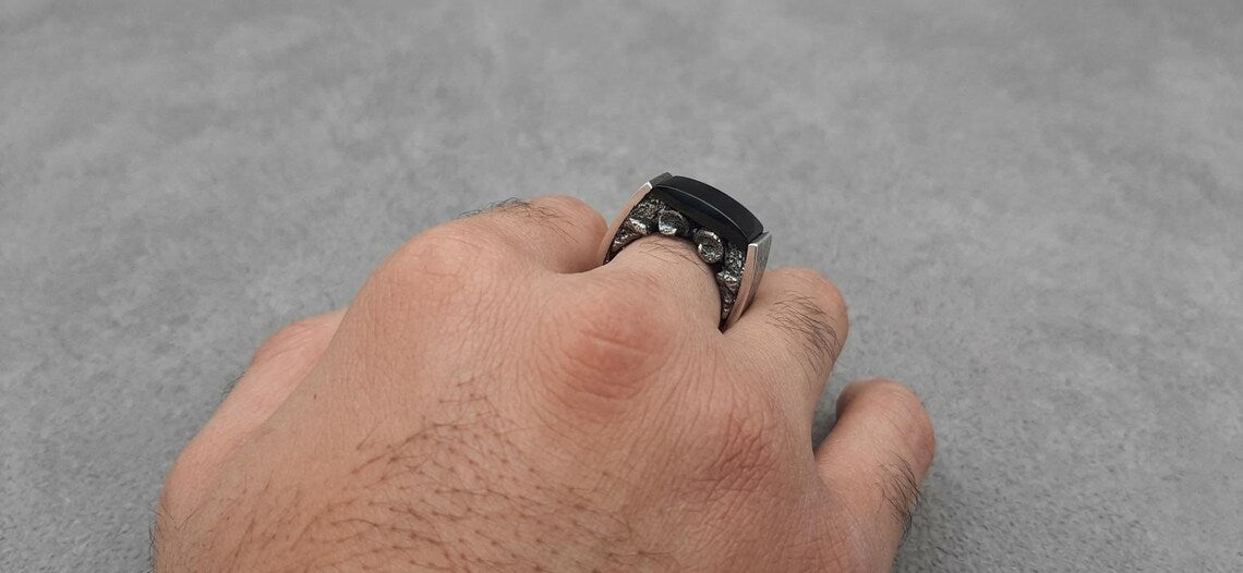 Hand wearing a black ring on a gray background