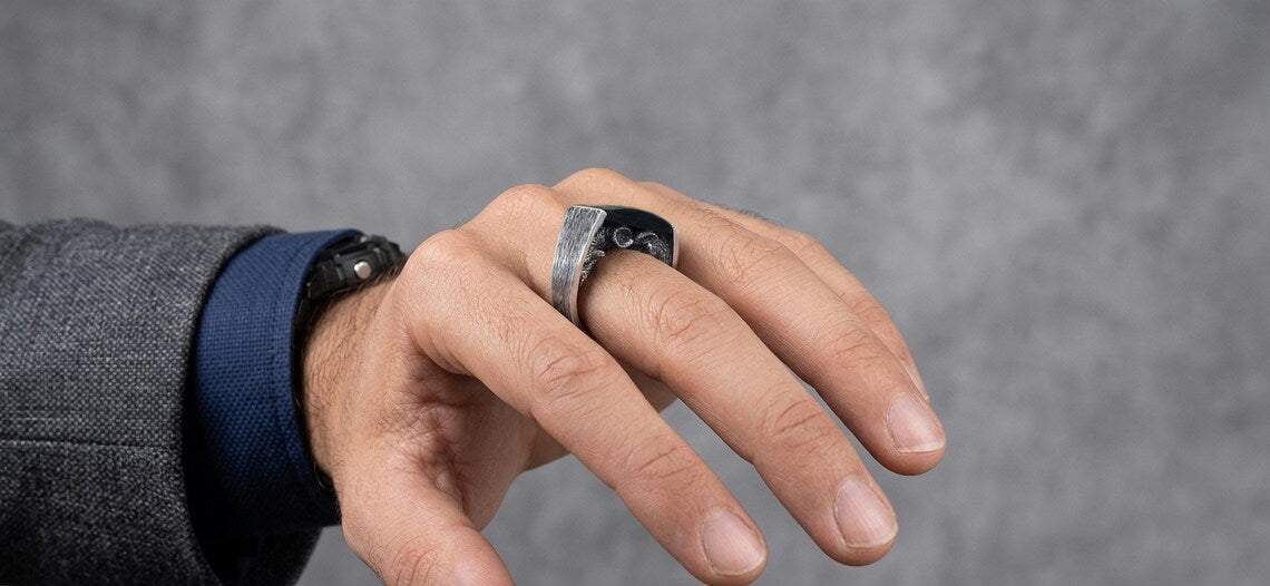 Hand wearing a silver ring on a gray background
